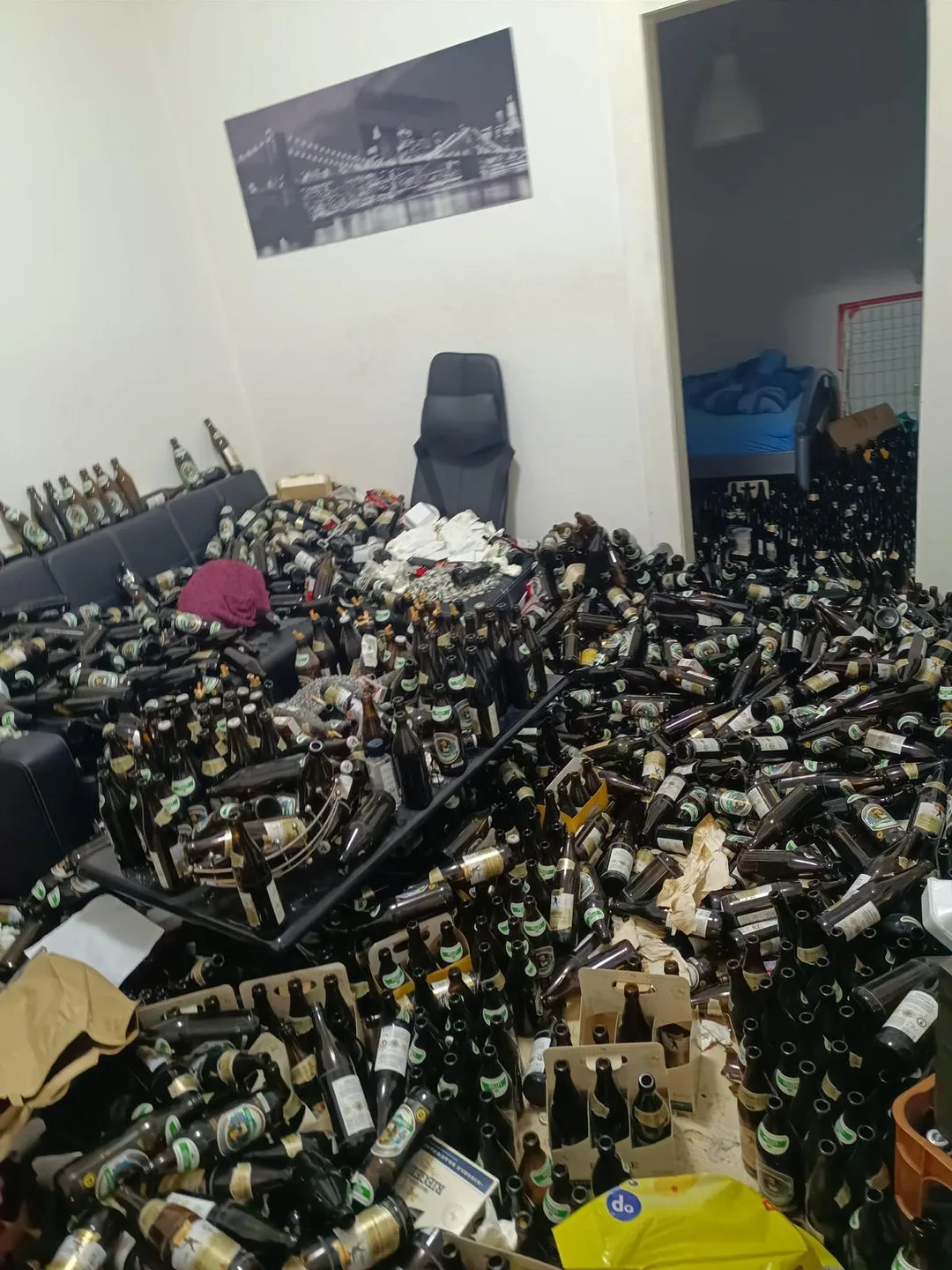 Dasselbe Wohnzimmer vor der Räumung: Boden und Sofa vollständig mit leeren Flaschen bedeckt